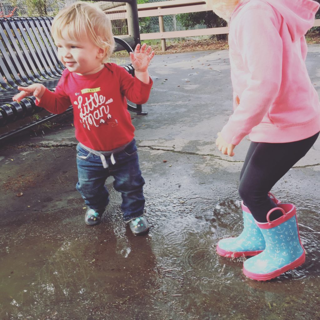 Two kids jumping in rain puddles