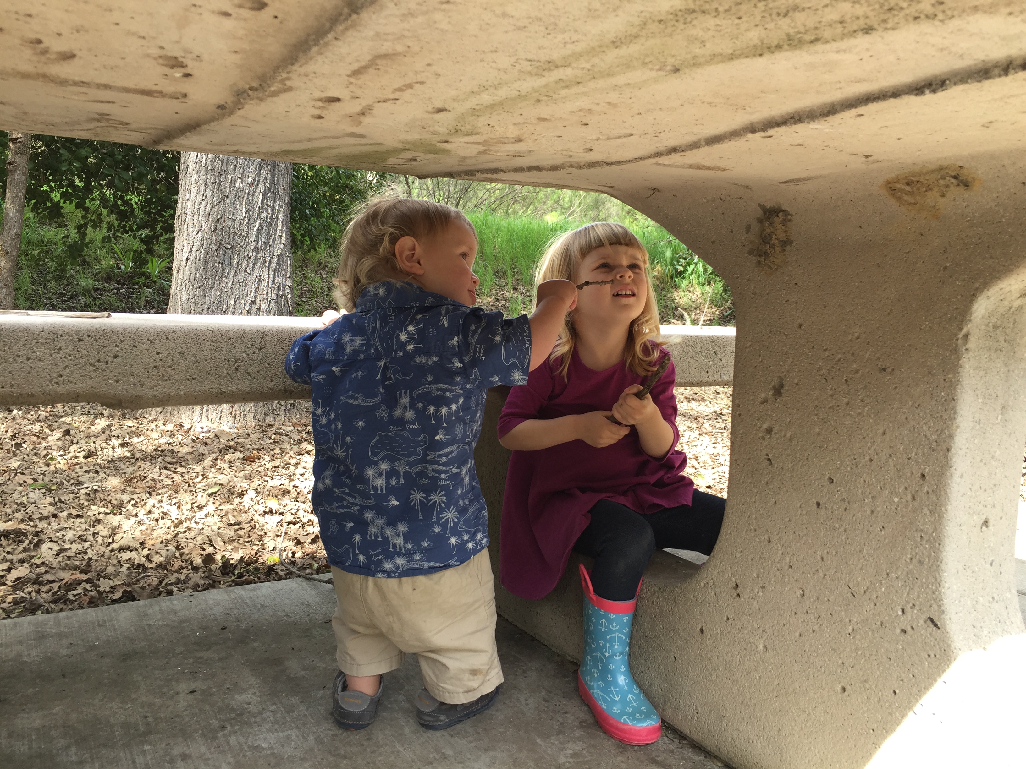 The kids under a concrete picnic table at Apple Valley Park in Atascadero California from the blog Two In Tow & On The Go.