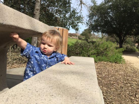 Baby exploring a concrete picnic table at Apple Valley Park in Atascadero California from the blog Two In Tow & On The Go.
