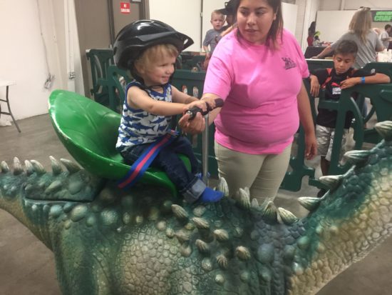 Baby on a walking dinosaur at Jurassic Quest Paso Robles 