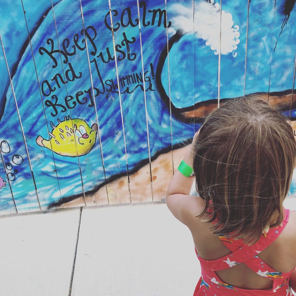 Little girl looking at a wall mural of a wave