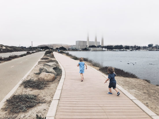 MORRO BAY HARBORWALKTwo In Tow & On The Go: A Family Adventure Column By Tonya Strickland __________________________________________________________________________ Two In Tow & On The Go is a SLO County Mommy Blog that details pictures, tips and stories about things to do with kids on California's Central Coast. Follow the adventure at @two.n.tow on Instagram and Facebook & at twontow.com. __________________________________________________________________________ On a whim, my 2 and 4 year old kiddos and I recently explored the Morro Bay HarborWalk. We were met with thrill-worthy beach swings, playful sea otters that tumbled and twirled in the calm harbor waters and boats that passed us as we ran along the expansive slated boardwalk. Kind of magical, right? This easy and free kidventure is a great way to get outside with a few key stops while you’re there. Once you walk the HarborWalk, you’ll find several lookout points, a slatted boardwalk and a Class 1 bike path away from the road. Between you start at the Embarcadero to the parking lot There are also two public restroom stops, a swing set and several lookout points with benches facing toward the calm waters. The humble beginnings of this stretch of Morro Bay was all just a vision In the early 1950s, according to the city. As the story goes, a Mr. Arthur E. Coleman worked to connect Morro Rock to the Embarcadero via a road to build a waterfront park for children. And that’s just what exists today. Coleman Park features a fenced basketball court and six swings (including two bucket swings for the babes! The accompanying HarborWalk, completed about a decade ago, stretches from the Embarcadero’s quaint string of gift/seafood/saltwater taffy shops to the iconic Morro Rock, the last in a line of volcanic earthly throwbacks reaching south toward San Luis Obispo. HarborWalk pairs a pedestrian walkway with slatted boards and a seperate, two-lane paved bike path for guests of all kinds. Even the crazy preschool-toddler variety. In fact, our favorite stop is a tie between the Coleman Park swingset and the playful otter pups swimming just south of the Rock As a bonus, it has lots of lookouts and views of harbor boats! And if you’ve studied up on your preschooler story books, you’ll know them aaaall the boat names. And that’s it! Easy-peasy. You could end your trip there, or go explore the Morro Bay Embarcadero which we detail in a Morro Bay Day Guide over on the blog, twontow.com; OR you can call it a success and just head home (I, personally, tend to not chance it with those tiny humans in tow). Either way, it will be fun day in Morro Bay. See you there!