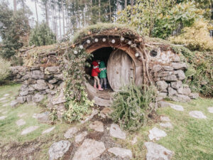 Two kids in coats standing at the entrance of a Hobbit House with round door