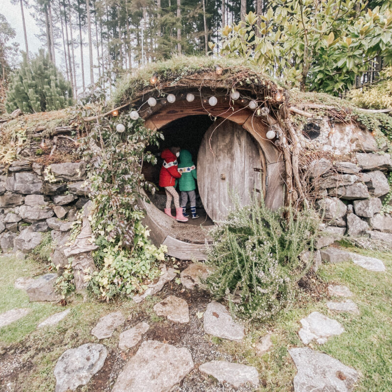 Two kids in coats standing at the entrance of a Hobbit House with round door