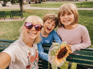 two kids smiling at park bench w/mom