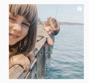 two kids leaning on wood railing over a pierr