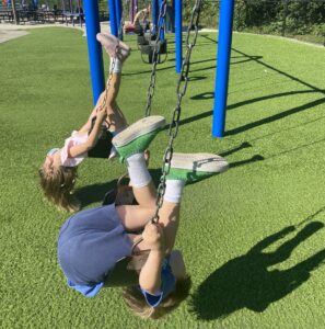 kids upside down on swings, green lawn below