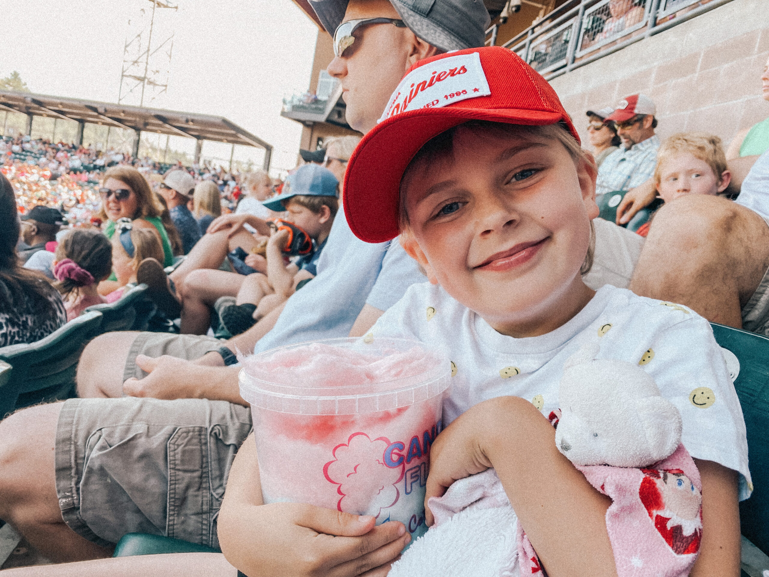 girl in a red hat holding a cotton candy tub and a stuffed bear.