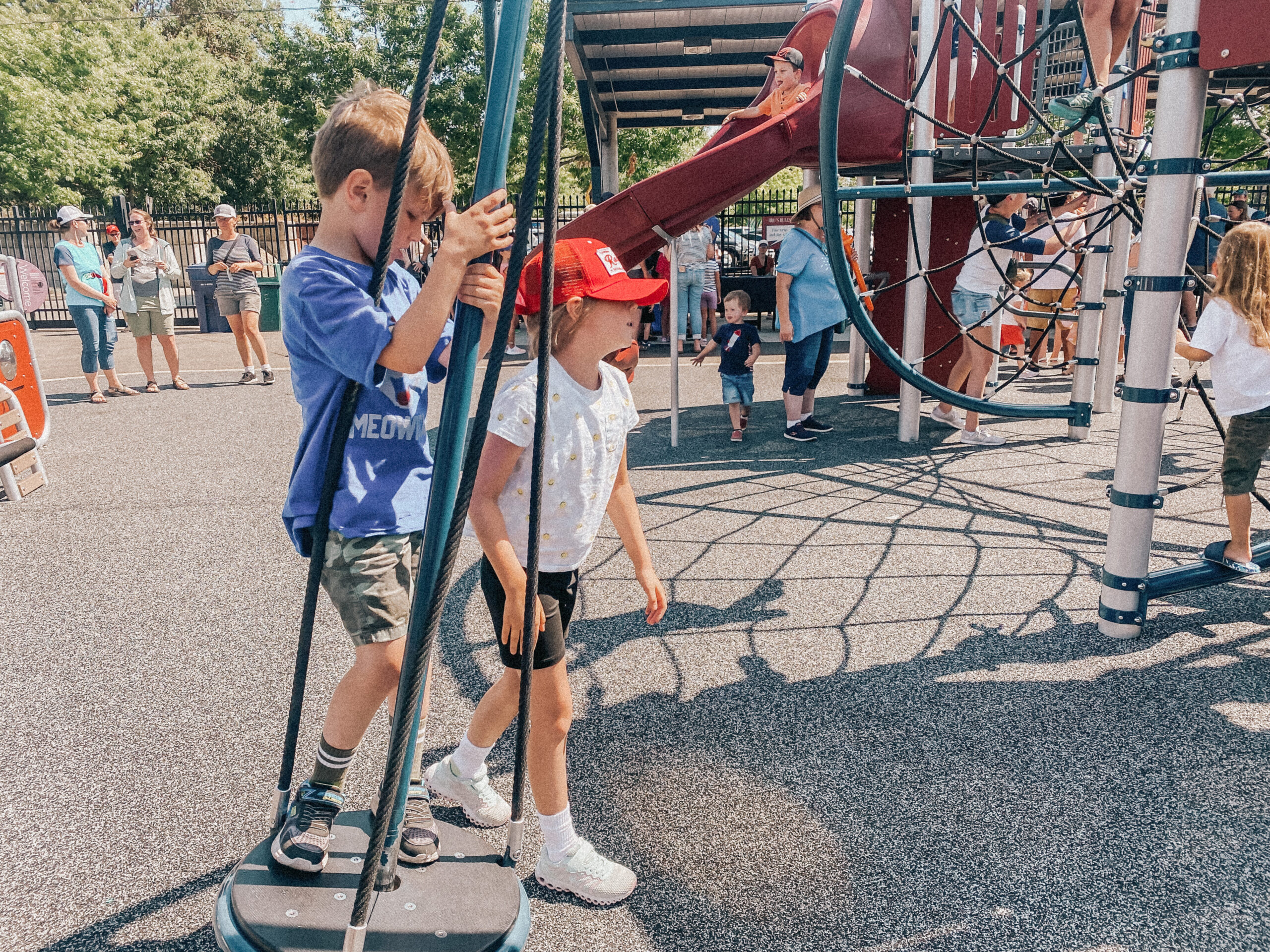 This is a photo a boy in a blue shirt and a girl in a red hat playing on a standing toy that spins at the playground at Cheney Stadium.